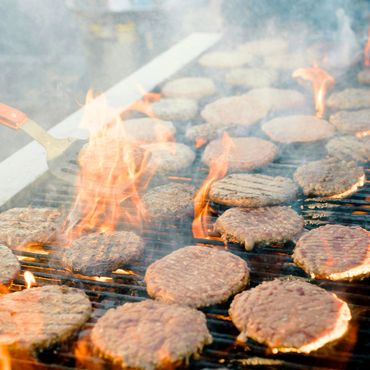 Cocinando varias hamburguesas de El Establo en un asador o parrilla con carbón o leña