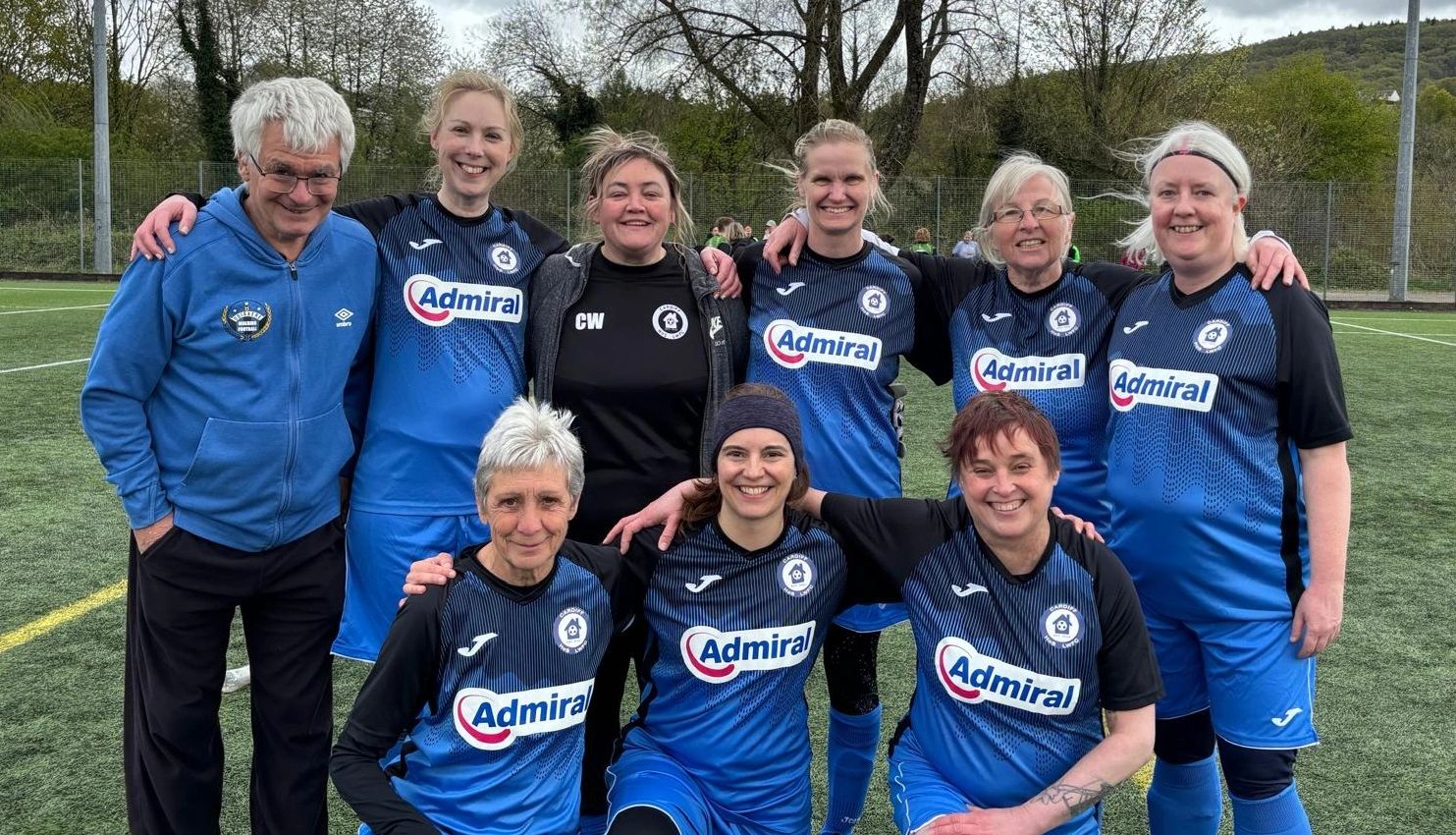 A happy Cardiff Walking football team posing together on a pitch.