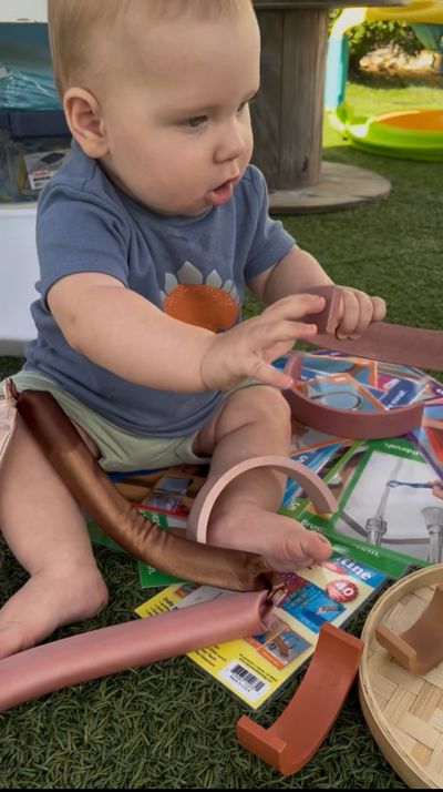 A baby playing with colorful foam pieces and magazines on grass.