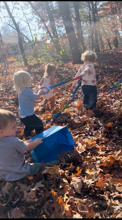 Children playing and digging in autumn leaves in a sunlit forest.