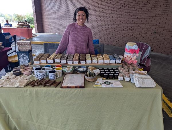 Woman selling homemade baked goods and crafts at a market stall.