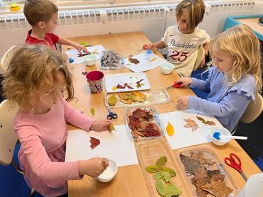 Children at a table making art with leaves