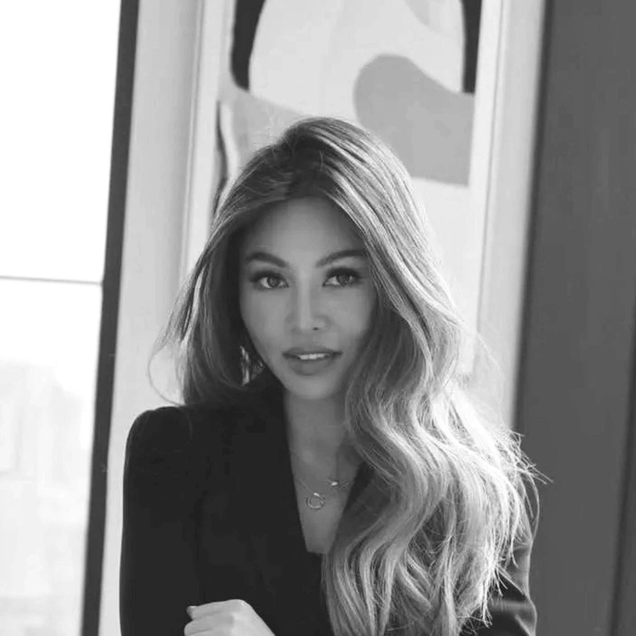 Confident woman with long wavy hair posing indoors near a window.