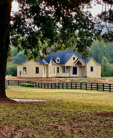 A beige house behind a black fence with trees in the foreground.