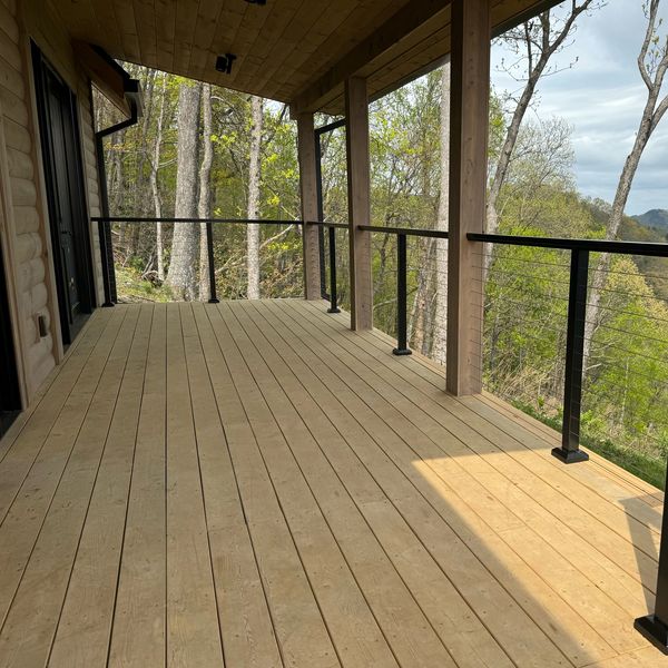 Empty wooden deck overlooking trees and hills.
