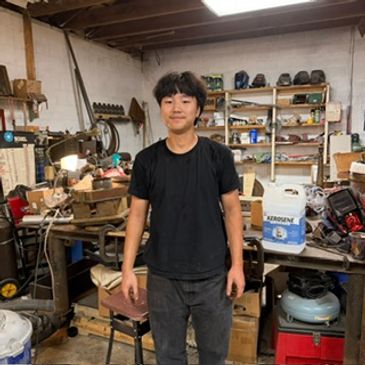 Young man standing in a cluttered workshop.