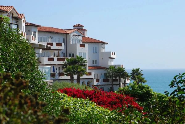 White building by the sea with lush greenery and flowers.