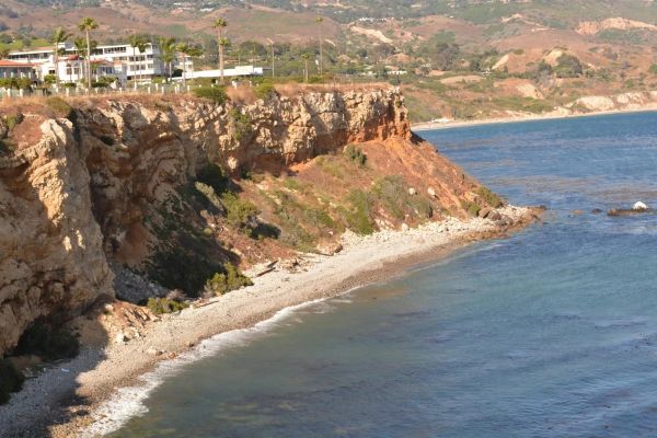 Cliffside beach with clear blue water and buildings above.