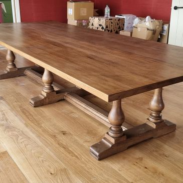A large wooden dining table with turned legs on a wooden floor.