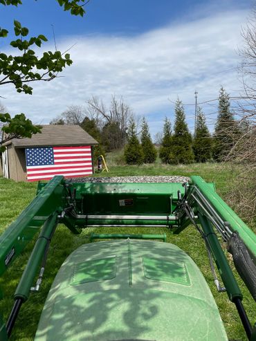 Modern green tractor for brush cutting with American flag barn art in background