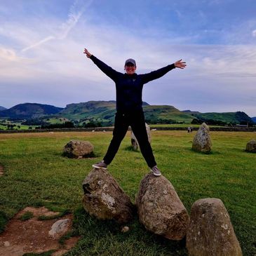 A woman standing on top of some stones at a stone circle. Happy smiling freedom, castlerigg
