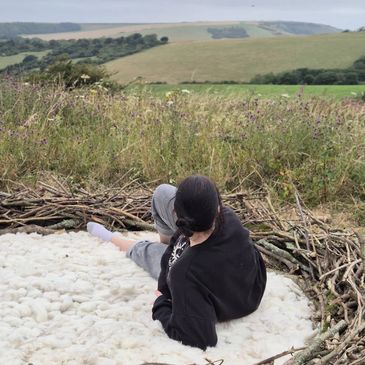 a woman laying in a nest made from branches and sheeps wool on top of a hill at butts brow in sussex