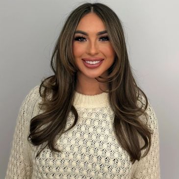 A smiling woman with long brown hair wearing a cream knitted sweater.