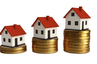 Three miniature houses on stacks of gold coins increasing in height.