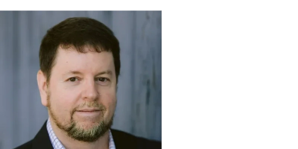 Professional headshot of a man with a beard and dark hair in a suit jacket.