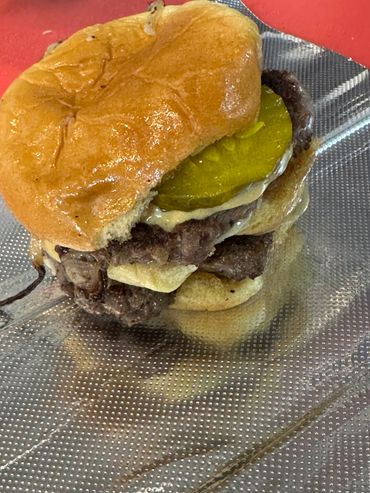 A partially eaten cheeseburger with pickles on a textured plate.