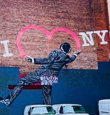 Mural of a suited man painting a pink heart on a brick wall with 'I ❤️ NY' text.