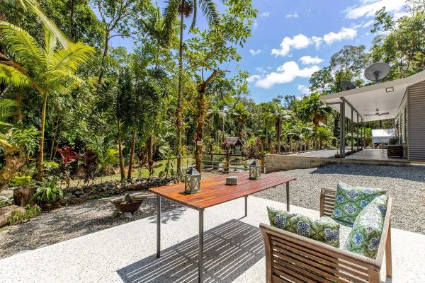 Sunny backyard patio with wooden table and tropical greenery.