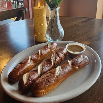 Three pretzel sticks with mustard dip on a white plate at a cozy table.