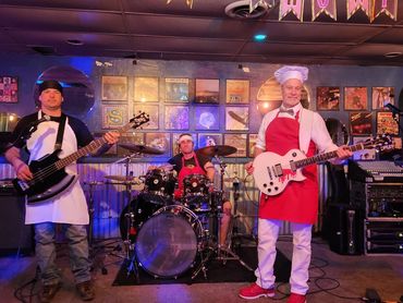Three musicians in aprons performing on stage with guitars and drums.