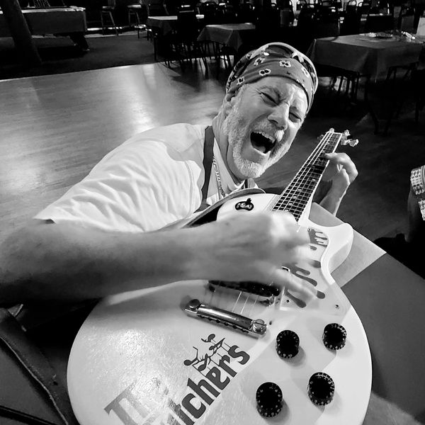 Joyful man passionately playing electric guitar in a lively setting.
