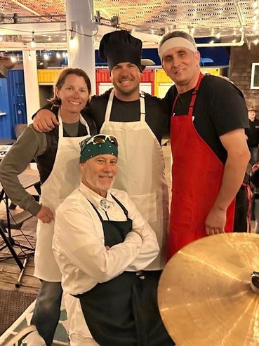 Four happy chefs posing together, wearing aprons and chef hats.