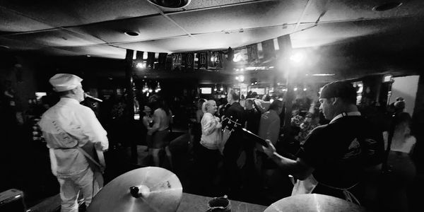 Black and white photo of a live band performing to a lively crowd in a small venue.