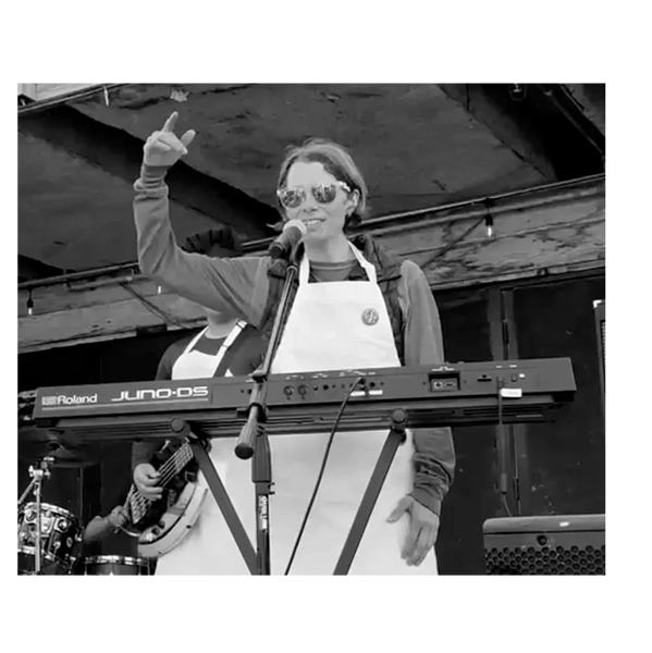 Musician wearing an apron and sunglasses plays keyboard on stage.