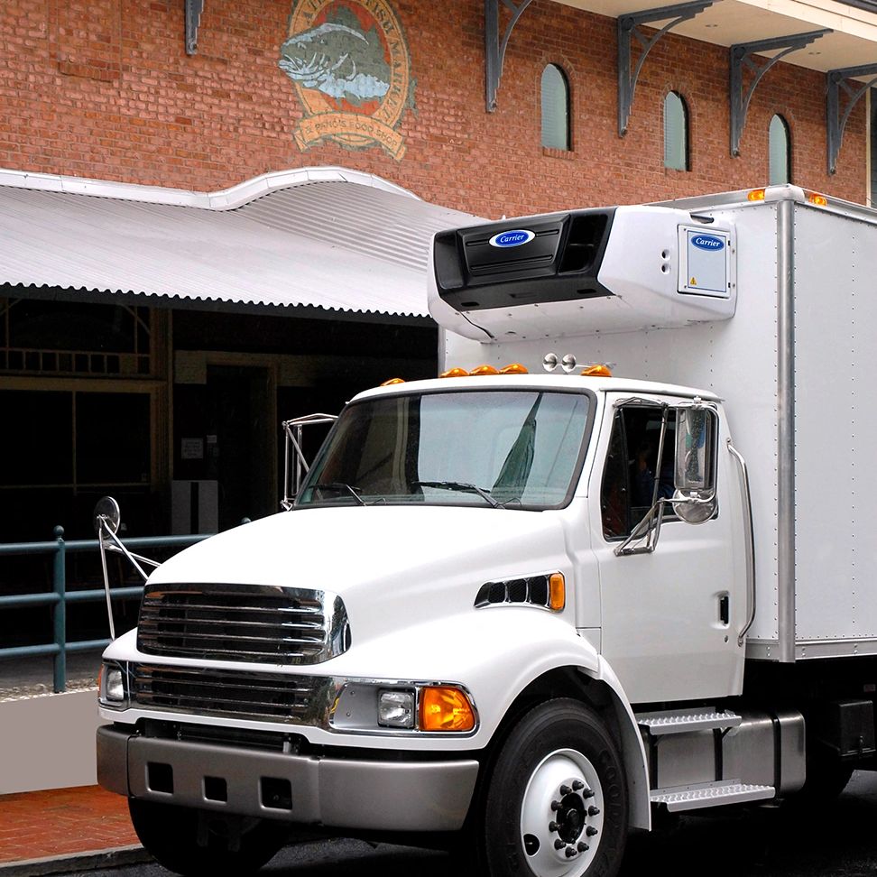White refrigerated delivery truck parked on street near brick building.