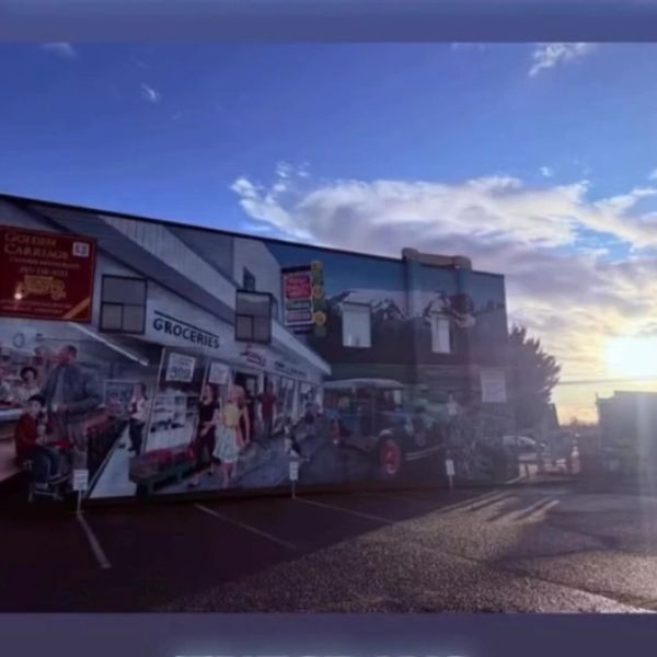 Sunset illuminates a detailed mural of a vintage grocery store scene on a building wall.