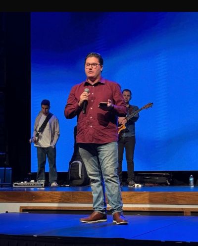 Man speaking on stage with musicians behind him.