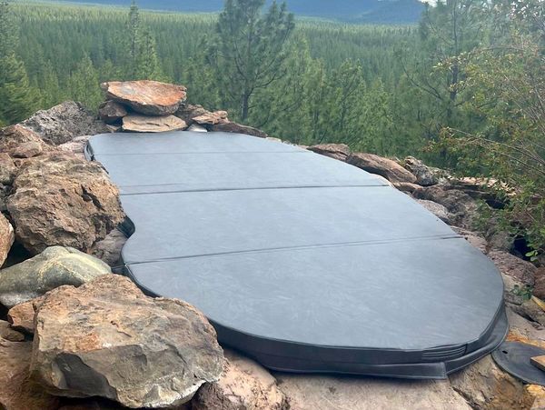 Custom-made black spa cover over rocks with trees as background.