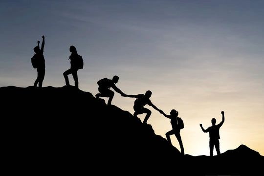 People helping each other climb a hill at sunset.