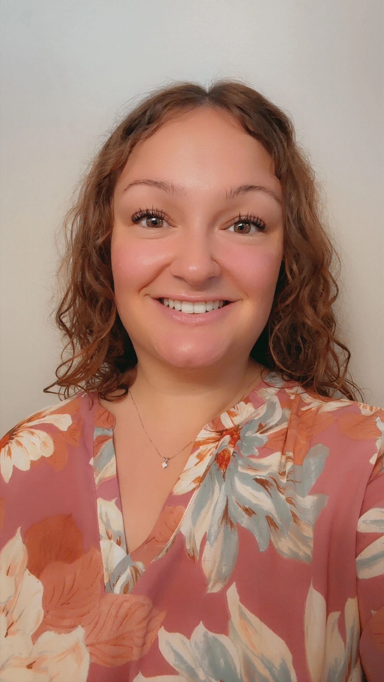 Smiling woman with curly hair in a floral blouse.