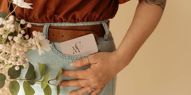 Person with flowers and a card in back pocket wearing denim and brown belt.