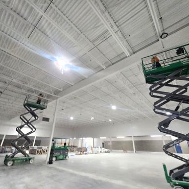 Scissor-lift installation of commercial warehouse lighting. Tenant improvement completed by VoltPro