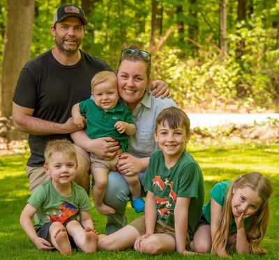 A happy family of six posing together outdoors in a green park.