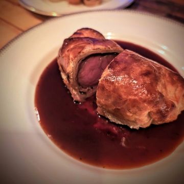Beef Wellington served with rich red wine sauce on a white plate.