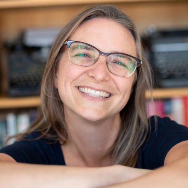 Smiling woman with glasses in cozy indoor setting.