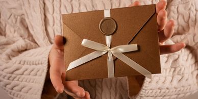 Hands holding a gift-wrapped envelope with a white ribbon.