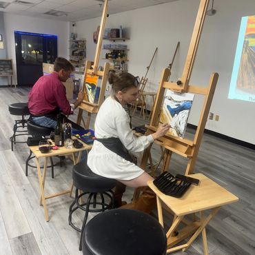Two people painting in art studio with easels.