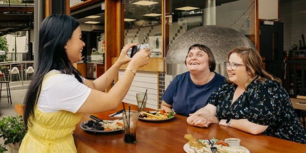 Three friends enjoying a meal together while one takes a photo.