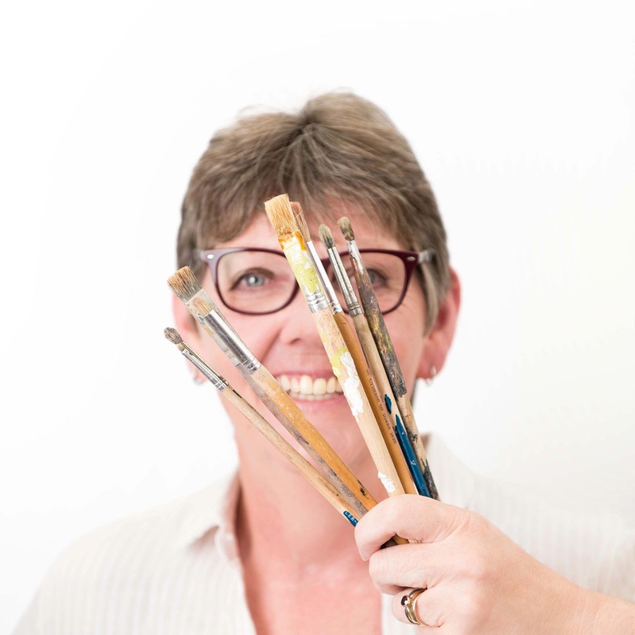 Happy woman holding paintbrushes in front of her face.