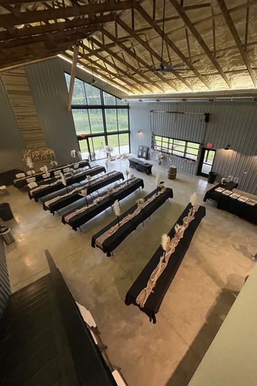 A rustic event space with long tables and black tablecloths decorated with beige runners and feathers.