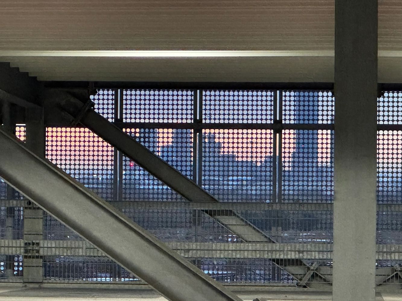 City skyline viewed through a perforated metal screen at sunset.