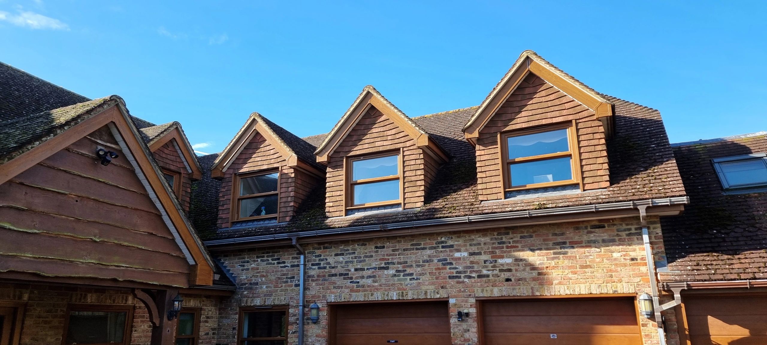 A brick house with three dormer windows under a clear blue sky.