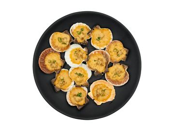 Baked scallops in shells on a black plate garnished with herbs.