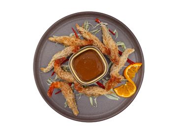Crispy fried shrimp with dipping sauce and orange slices on a gray plate.