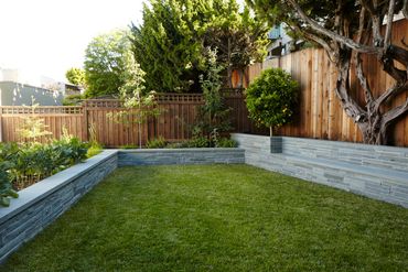 Modern backyard with lush grass, stone seating walls, and a wooden fence.
