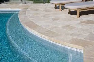 Curved pool steps leading into clear blue water beside beige stone pool deck.